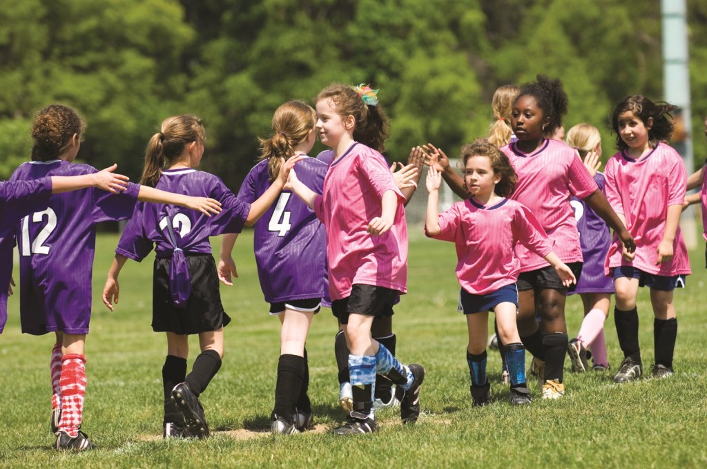 Stock photo of girl soccer players showing good sportsmanship at the end of a game. Purple and Pink teams congratulate each other on a game well played. Girls are in the 8 to 10 age group and of diverse backgrounds and cultures. Ten girls are in the image with four faces visable.